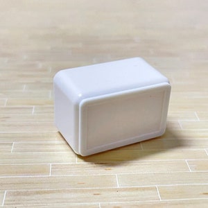 May include: A white rectangular box with a raised edge around the front. The box is made of plastic and has a smooth surface.