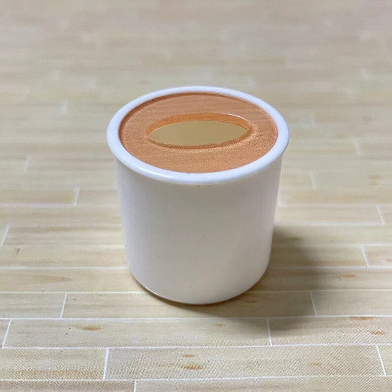 May include: A white ceramic cup with a light orange rim and a gold oval cutout in the center.