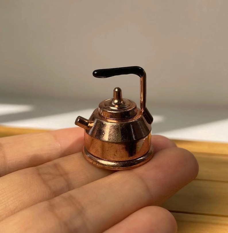 Pu&ograve; includere: Un piccolo bollitore di rame con un manico nero. Il bollitore &egrave; grande circa come la punta di un dito.