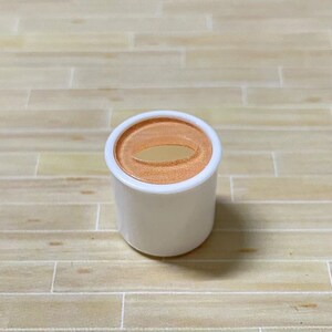 May include: A white plastic container with a round, orange lid. The lid has a small, oval-shaped opening in the center.
