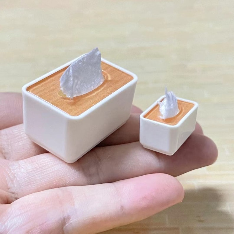 May include: Two white tissue boxes with orange interiors. The larger box has a white tissue inside, and the smaller box has a white tissue inside.
