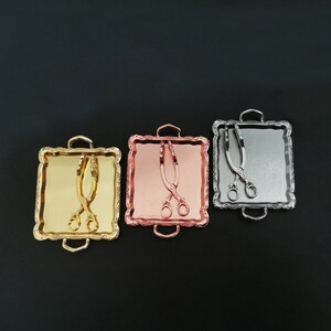 May include: Three miniature serving trays with handles, each featuring a different metallic finish: gold, rose gold, and silver. Each tray includes a pair of miniature tongs.