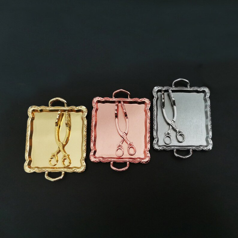 May include: Three miniature serving trays with handles, each featuring a different metallic finish: gold, rose gold, and silver. Each tray includes a pair of miniature tongs.