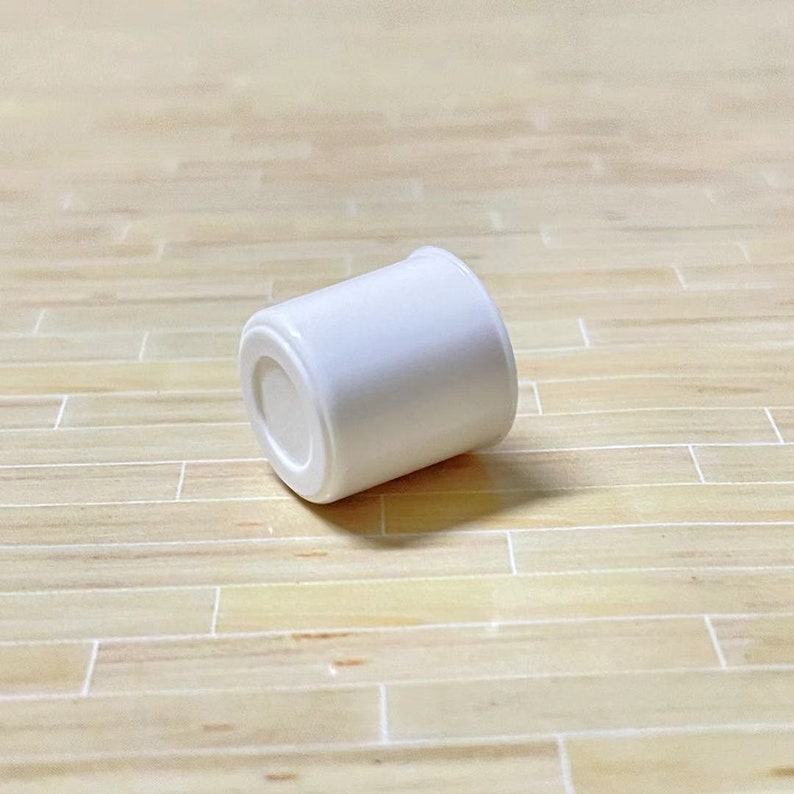 May include: A white plastic container with a smooth, rounded surface. The container is lying on its side on a light brown wooden surface.