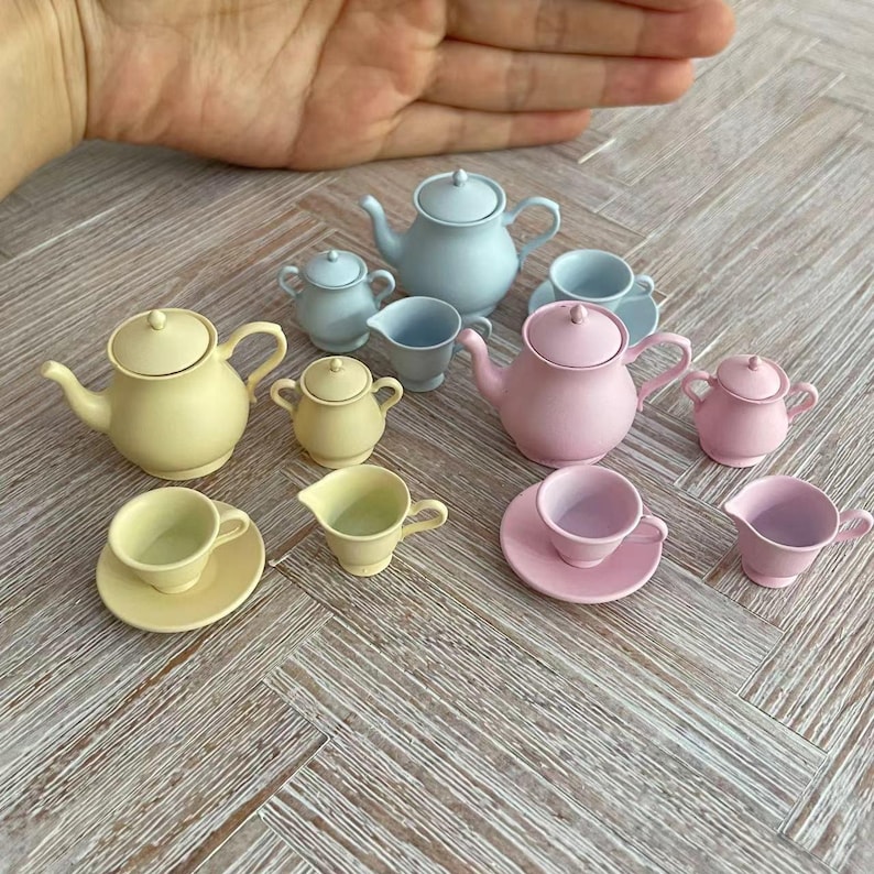 May include: A set of pastel-colored teacups, saucers, teapots, and creamer pitchers. The set includes light blue, light pink, and yellow pieces.