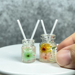 May include: Two clear glass jars with white straws, filled with a clear liquid and dried flowers. One jar has a pink and yellow flower, the other has a green flower.