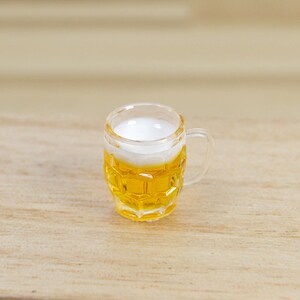 May include: A clear glass beer mug with a handle, filled with a golden yellow beer and a white head of foam.