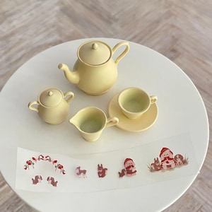 May include: A yellow tea set with a teapot, creamer, sugar bowl, and teacup and saucer. The set is on a white surface with a sheet of stickers featuring cartoon animals and people.