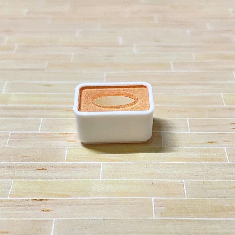 May include: A small white square box with a rounded top and a rectangular opening in the centre. The opening is surrounded by a light orange border.