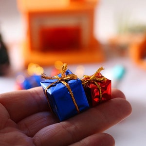 Könnte beinhalten: Zwei kleine Geschenkboxen, eine blaue und eine rote, mit goldenen Bändern und Schleifen. Die Boxen liegen auf einer Hand.