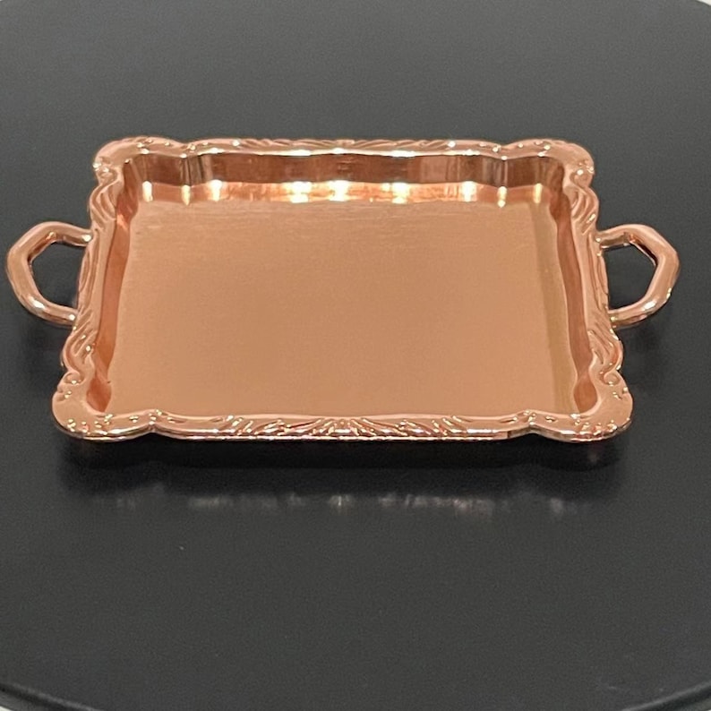 May include: A square copper serving tray with two handles. The tray has a decorative, ornate border.