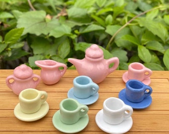 Puede incluir: Un juego de té en miniatura con una tetera rosa, una jarra de crema, un azucarero y seis tazas de té y platillos de colores pastel.