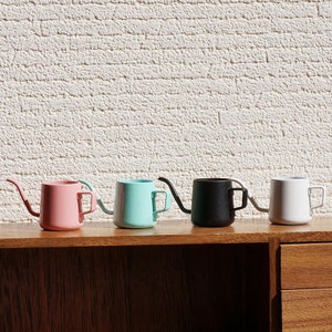 May include: Five small metal teapots in different colors: pink, light blue, black, white, and gray. The teapots are lined up on a wooden shelf.