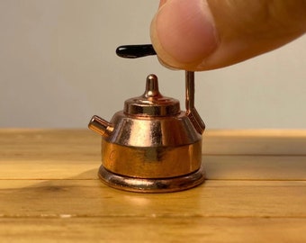 May include: A miniature copper teapot with a black plastic handle. The teapot is sitting on a wooden surface.