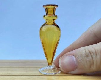 May include: A small amber glass vase with a clear glass base. The vase has a rounded body and a narrow neck.