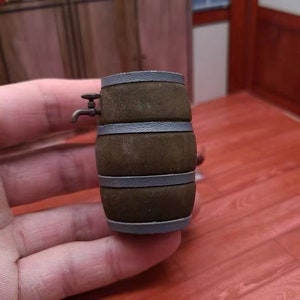 Pode incluir: Um pequeno barril de madeira com uma torneira de metal, pintado de marrom com faixas cinzas. O barril est&aacute; sobre uma superf&iacute;cie de madeira.
