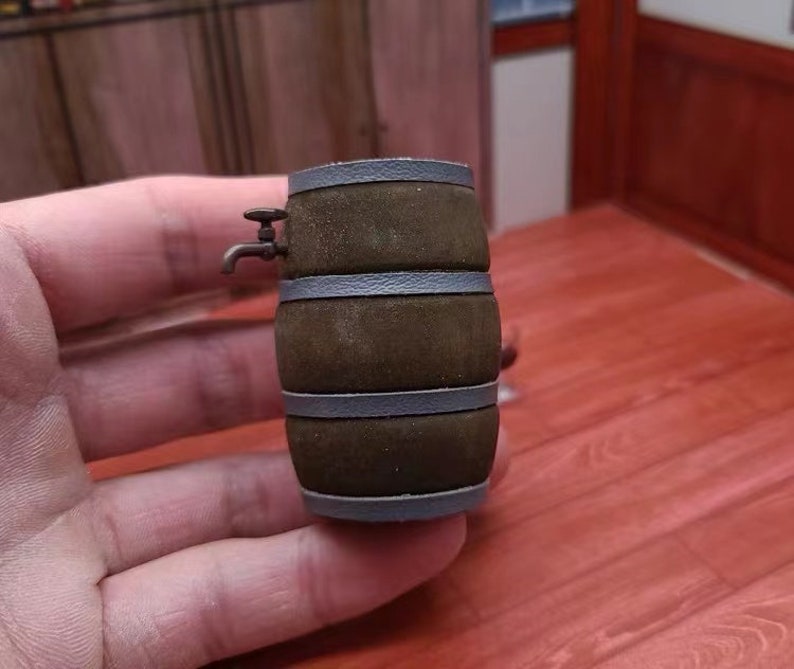 Pode incluir: Um pequeno barril de madeira com uma torneira de metal, pintado de marrom com faixas cinzas. O barril est&aacute; sobre uma superf&iacute;cie de madeira.