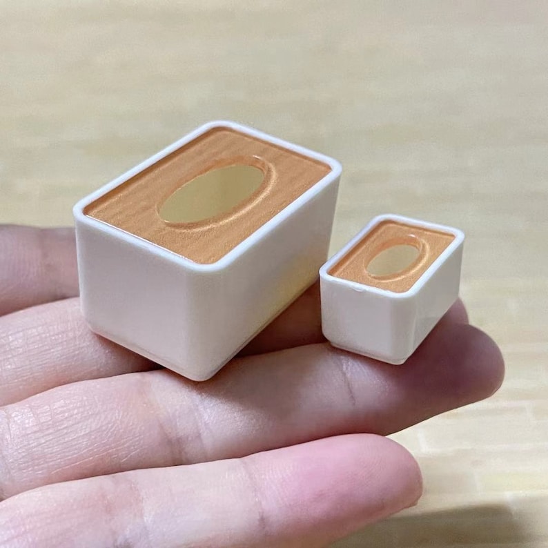 May include: Two white plastic boxes with orange lids. The boxes are rectangular in shape and have a small oval opening in the lid. The larger box is in the foreground and the smaller box is behind it.
