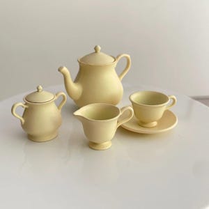 May include: A yellow tea set with a teapot, creamer, sugar bowl, and a cup and saucer.