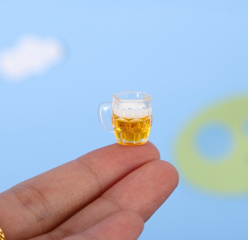 May include: A miniature glass beer mug filled with a light yellow beer with a white head.