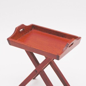 May include: A wooden folding tray table with a reddish-brown finish. The tray has a raised edge and two handles on the sides. The table is made of four legs that fold up for storage.