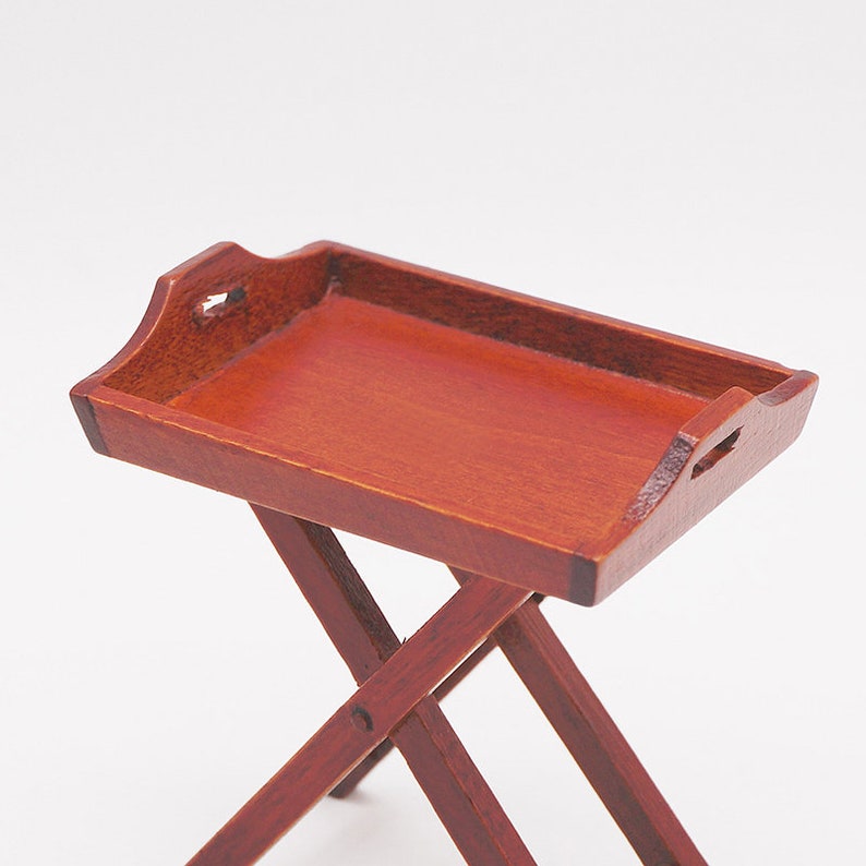 May include: A wooden folding tray table with a reddish-brown finish. The tray has a raised edge and two handles on the sides. The table is made of four legs that fold up for storage.