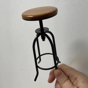 May include: A small wooden and black metal stool with a round seat. The stool is adjustable in height.