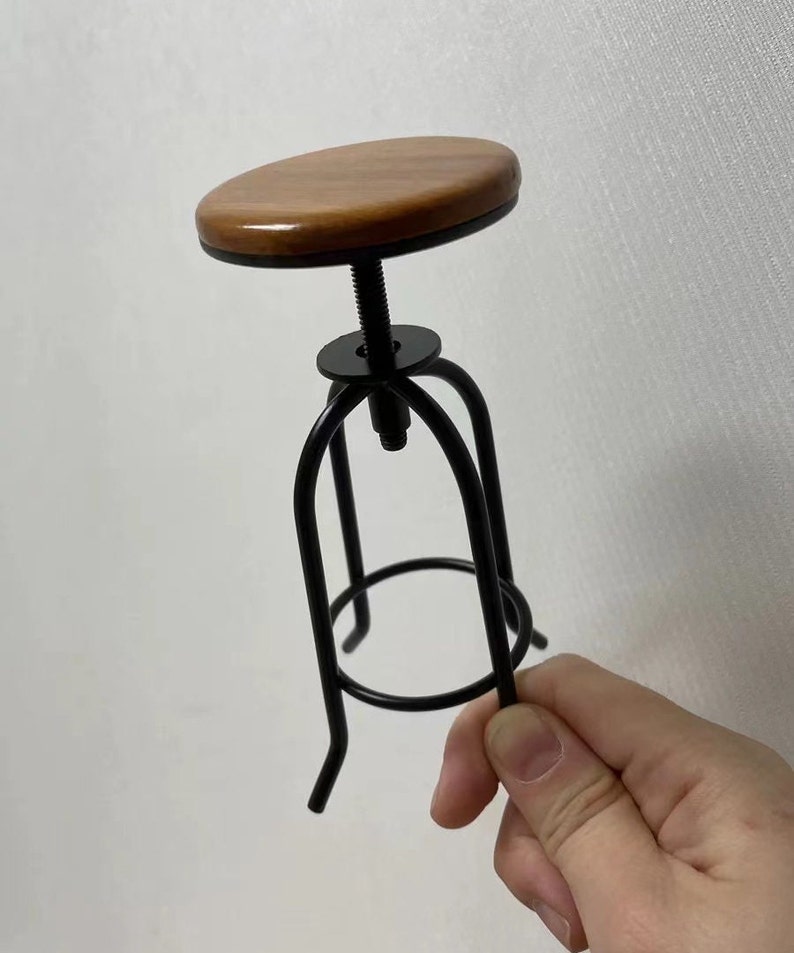May include: A small wooden and black metal stool with a round seat. The stool is adjustable in height.