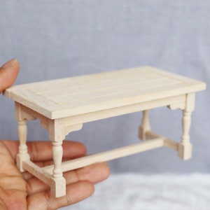 Puede incluir: Una pequeña mesa de madera sin terminar con una tapa rectangular y cuatro patas. La mesa está hecha de madera de color claro y tiene un diseño simple y rústico.