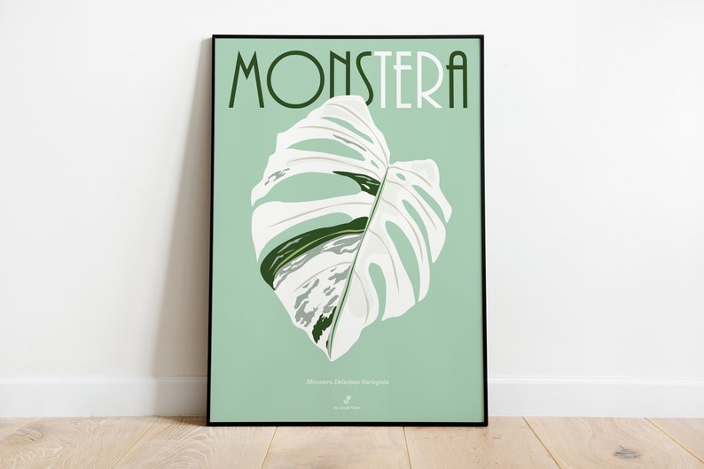 May include: A poster with a green background and a white Monstera Deliciosa variegata leaf. The text "MONSTERA" is in black letters at the top of the poster.