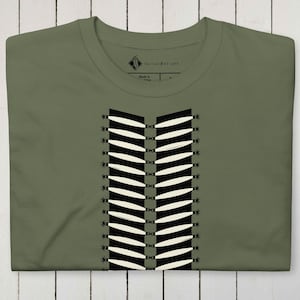 Può includere: Una maglietta verde con un design geometrico in bianco e nero. Il design presenta una serie di forme intrecciate che ricordano un motivo tessuto. La maglietta ha un collo rotondo e maniche corte.
