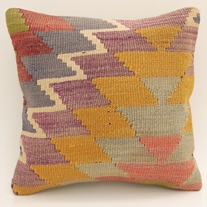 Puede incluir: Una almohada de tiro colorida con un patrón geométrico en tonos de morado, amarillo, rosa y gris. La almohada está hecha de tela tejida y tiene un diseño tradicional.