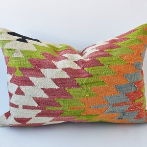 May include: A colorful throw pillow with a geometric pattern in shades of red, green, orange, and gray. The pillow is made of a woven fabric with a textured surface.