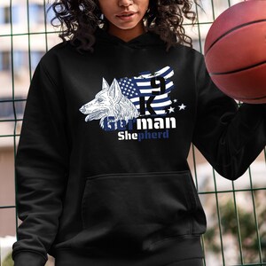 Może przedstawiać: Czarna bluza z kapturem z białym nadrukiem niemieckiego owczarka z niebiesko-białą flagą amerykańską i tekstem "9K German Shepherd".