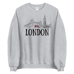 May include: A gray sweatshirt with a black and white illustration of the London skyline, including Big Ben and Tower Bridge, with a red double-decker bus driving across the bridge. The text "LONDON" is printed in black below the illustration.