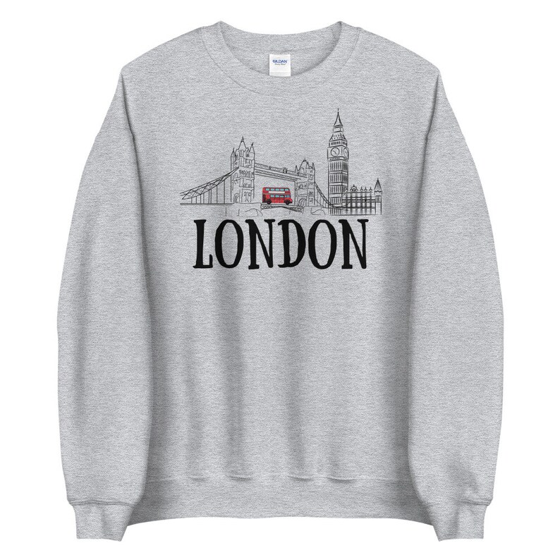 May include: A gray sweatshirt with a black and white illustration of the London skyline, including Big Ben and Tower Bridge, with a red double-decker bus driving across the bridge. The text "LONDON" is printed in black below the illustration.