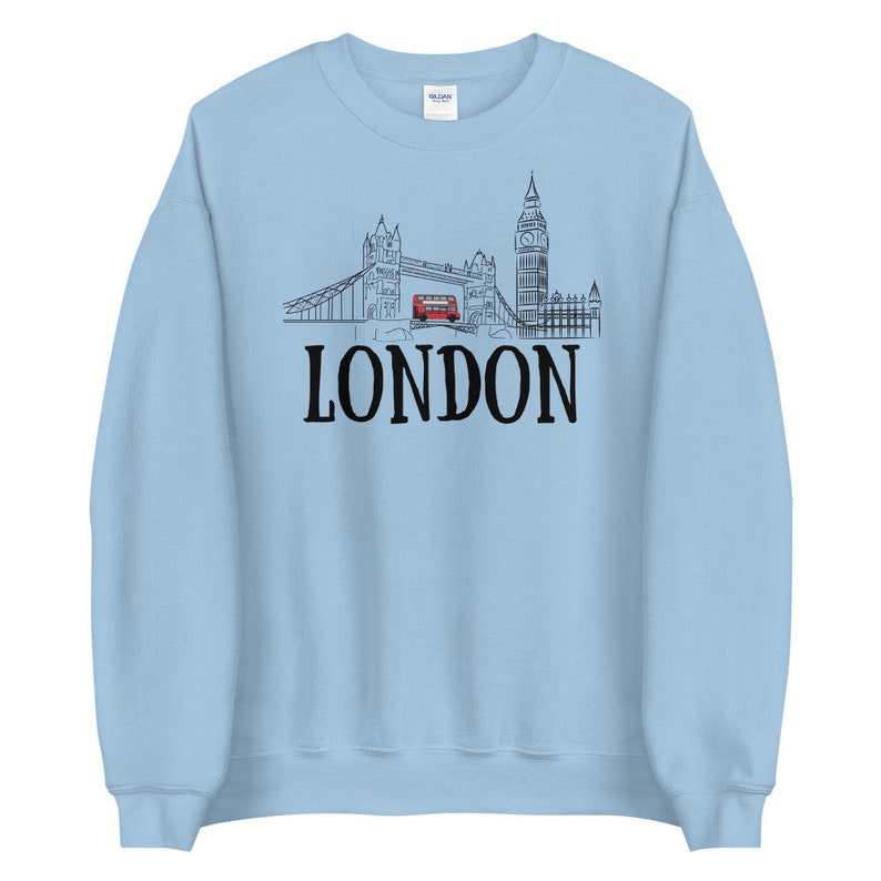 May include: A light blue sweatshirt with a black and white illustration of the London skyline, including Big Ben, Tower Bridge, and a red double-decker bus. The text "LONDON" is printed in black below the illustration.