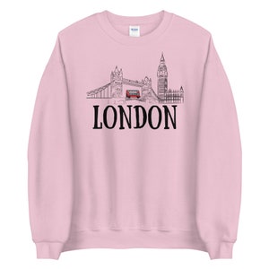 May include: Pink sweatshirt with a black outline of the London skyline, including Big Ben, Tower Bridge, and a red double-decker bus. The word "LONDON" is printed in black below the skyline.