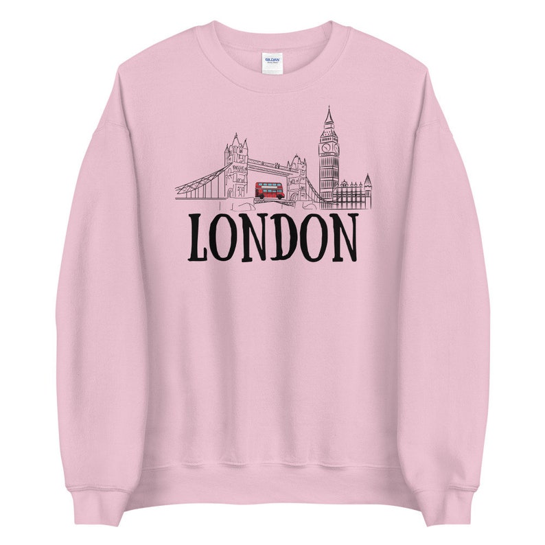 May include: Pink sweatshirt with a black outline of the London skyline, including Big Ben, Tower Bridge, and a red double-decker bus. The word "LONDON" is printed in black below the skyline.