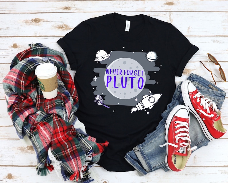 May include: Black t-shirt with a white and gray graphic of a moon with the text "Never Forget Pluto" in purple letters. The graphic also includes a rocket, a spaceship, and stars.