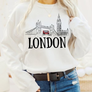 May include: White sweatshirt with a black and white illustration of the London skyline, including Big Ben and Tower Bridge, with a red double-decker bus. The text "LONDON" is printed below the illustration.
