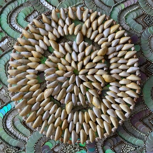 May include: A circular design made of small, white and cream-colored seashells arranged in a spiral pattern. The seashells are set against a background of green and silver sequins.