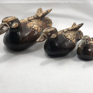 May include: Three wooden duck figurines, each with a different size. The ducks are painted brown with white accents and have a detailed design.