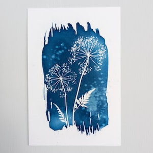 Pode incluir: Uma impressão botânica com silhuetas florais e de samambaias brancas sobre um fundo azul escuro. A obra de arte é apresentada em papel branco, criando um contraste marcante. A imagem tem uma aparência texturizada e artística.