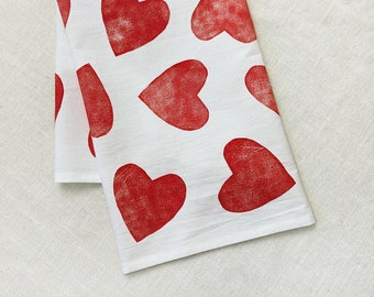 Peut inclure: Serviette de cuisine blanche avec un motif de cœurs rouges. Les cœurs sont imprimés dans un style vieilli, donnant à la serviette un aspect vintage.