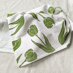 May include: A white kitchen towel with a green floral print of tulips. The towel is folded and has a textured surface.