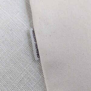 Pu&ograve; includere: Primo piano di un'etichetta in tessuto bianco con il testo "ORGANIC COTTON" stampato in nero.