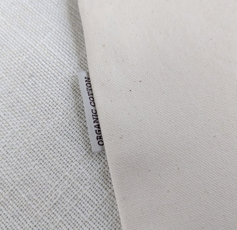 Pu&ograve; includere: Primo piano di un'etichetta in tessuto bianco con il testo "ORGANIC COTTON" stampato in nero.