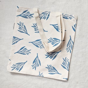 May include: A white canvas tote bag with blue leaf print and natural cotton straps.