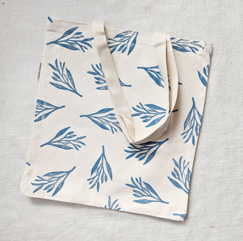 May include: A white canvas tote bag with blue leaf print and natural cotton straps.